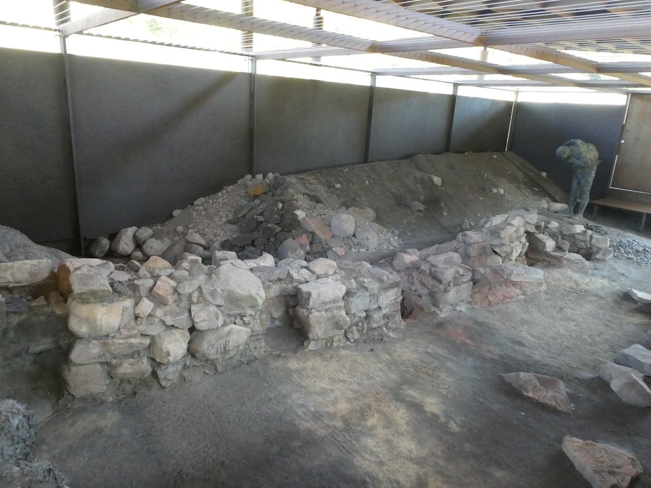 … schützt und präsentiert Verhüttungsanlagen der Bronzezeit. Man sieht auf diesem Foto die nischenartigen Hohlräume der Schachtöfen in der Mauer (die Vorderseite wurde nach dem Verhütten herausgebrochen). Rechts im Hintergrund ist schematisch ein Handwerker dargestellt (Foto: LWL-Archäologie für Westfalen/Manuel Zeiler).
