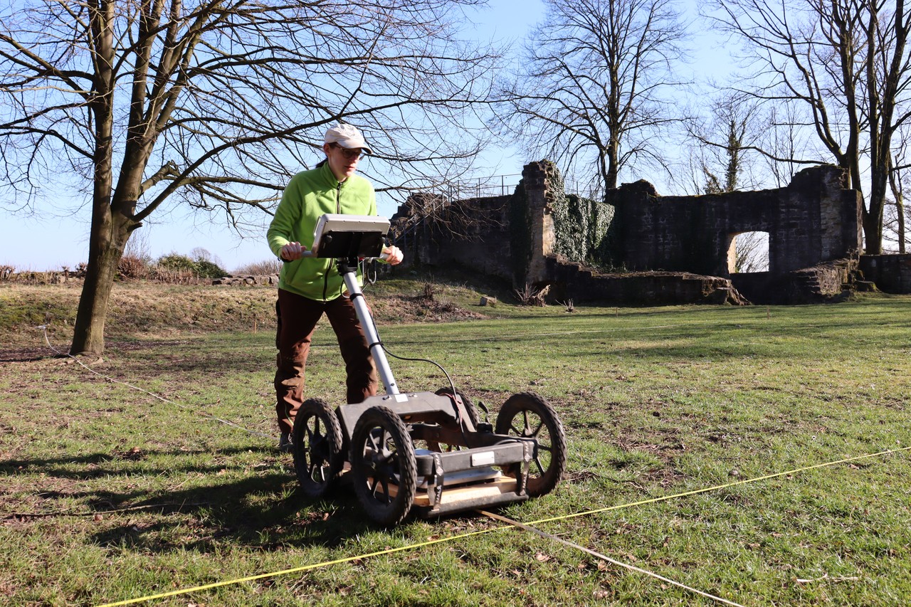 Eine Mitarbeiterin der Prospektion schiebt einen Wagen mit Bodenradar vor sich über den Innenhof der Burg.
