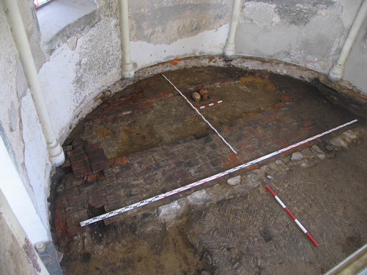 Blick von einem Baugerüst in die Kapellenapsis mit den beiden menschlichen Schädeln sowie Resten der historischen Fußbodenbeläge, u. a. ausgeführt als Spicksteinpflasterung-