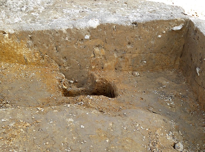 Profilschnitt durch ein Grubenhausbereich mit einem Pfostenloch. Während sich die Pfostenlochverfärbung links deutlich von anstehenden gelben Lehm absetzt, ist die braune Verfüllung des Grubenhauses rechts vom anstehenden gelbbraunem Lehmboden wenig gut zu erkennen. Foto: LWL-Archäologie für Westfalen/S. Spiong