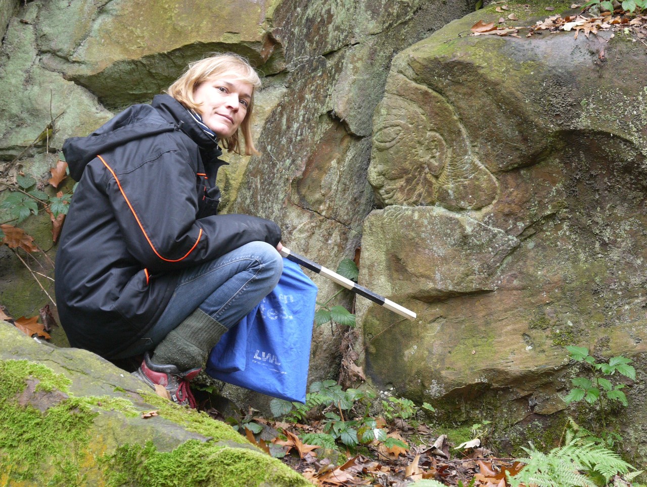 Eva Cichy bestaunt das ungewöhnliche menschliche Antlitz im Ruhrsandstein - Foto: M. Baales/LWL-AfW Olpe.